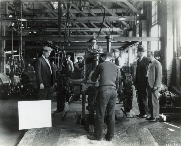 "'Pop Sohner' drives one of the early Farmall tractors off the end of the assembly line back in the 1920's. He pioneered the production of this all-purpose tractor at Farmall Works in Rock Island." Other men are standing around Pop and the tractor.