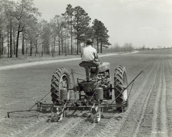 Rear view of a man driving a Farmall H tractor with H-100 corn planter in a field.