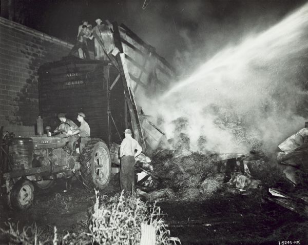 Two men on a Farmall M tractor are moving a railroad car loaded with alfalfa meal away from a fire at Piehl Alfalfa Mill.