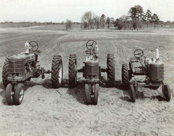 Slightly elevated view from front of Farmall tractors parked in a field. From left to right: Farmall M, Farmall H, Farmall A.