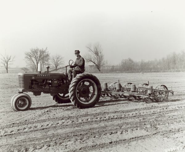 Left side view of a man driving a Farmall H in a field with a FA-114 four row planter.
