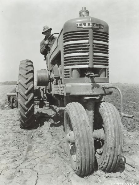 Front view of a man driving a Farmall M tractor 8 ft. 9-A double harrow in a field. Ross McKinstry farm.
