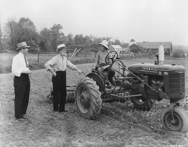 Clayton Nissley, Jr. sits on a Farmall B tractor. Standing next to him, left to right, are R.C. Northamer, sales promotion, general line, Harrisburg; and J.B. Hostetter of J.B. Hostetter & Sons, dealer of Mount Joy.