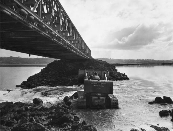 TD-14 in New Zealand bridge construction. Original caption reads: "The Bailey bridge provided access to the incompleted portion of the bank and was built over the deepest channel in the harbour. A TD-14 Drott takes like 'a duck to water' as the channel depth is decreased by placing rock under the bridge as a the bank level is built up."