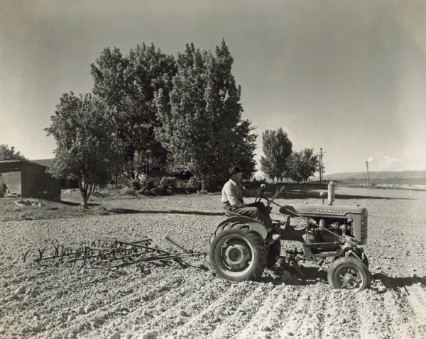 Right side view of a man driving a Farmall A tractor with an 8 foot spring tooth harrow. A.M Jensen.