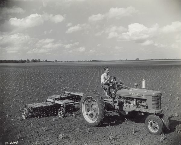 Three-quarter view from right side of Paul Meyer driving a Farmall H tractor with two McCormick-Deering rotary hoes to speed up corn hoeing.