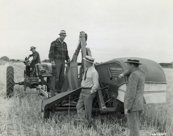 Four men posing with a Farmall H tractor pulling a No. 42 combine in a field in the Snake River Valley. The tractor and combine were being demonstrated in a 6-acre field of barley on the 80-acre farm of W.P. Taylor. Boyd Sorenson is on the tactor. Mr. Taylor is on the combine. Standing, on the left, is R.B. Corey of Corey Implement Company, which owns the Farmall H tractor and the No. 42 combine, and on the right, blockman P.W. Hussey.