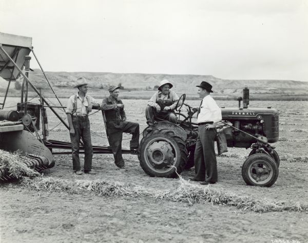 Four men are standing with a Farmall A tractor pulling a No. 61 combine in a field of Great Northern beans on 110-acre farm of Ralph Lyda. The outfit is owned by T.A. Wilder, a neighbor. From left to right are Mr. Lyda, Mr. Wilder's combine operator; John Carlson, Jr.; Mr. Wilder, and M.W. Jones, sales promotion, Billings branch.