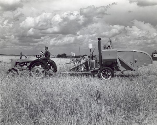 Left side profile view of a man driving a Farmall H tractor pulling a No. 62 combine on the farm of L.O. Norquist.