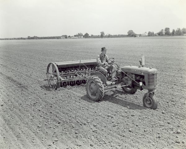 Slightly elevated three-quarter view from front right of Ray Whetstone drilling soybeans with Farmall B tractor and 13-7 McCormick-Deering fertilizer drill.