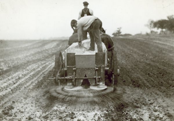 Rear view of two men with a horse-drawn end-gate lime spreader working in a field.