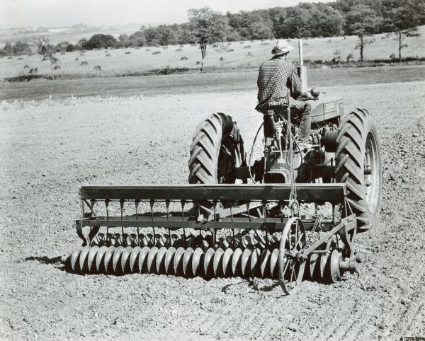 Rear view of a man using a Farmall M tractor with No. 58 double-gang soil pulverizer and grass seeding attachment. Taken at U.S. Soil Conservation Service demonstration.
