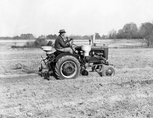 Right side view of man driving a Farmall A tractor with mounted planter fertilizer in a field.