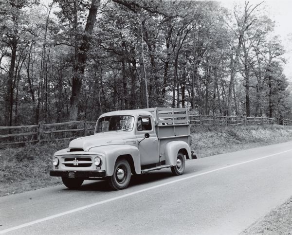 Three-quarter view from front of driver's side of R-110 Truck with pickup body traveling along a road. The bed has raised sides with gates, and two animals, perhaps cows or cattle, standing in the bed.