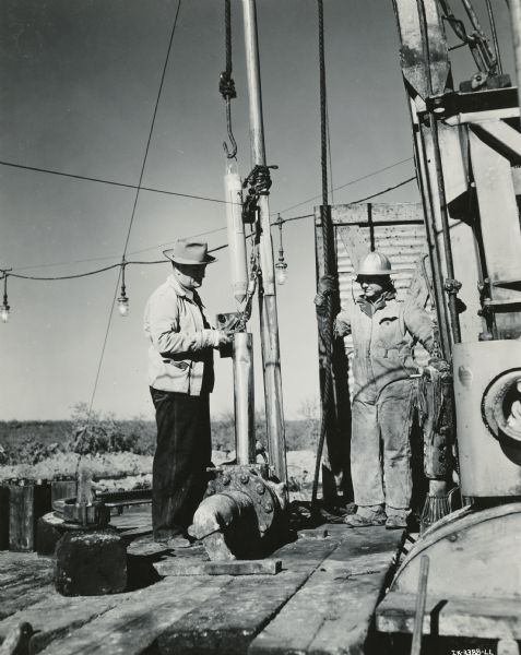 Two men are standing on the platform of an oil well.