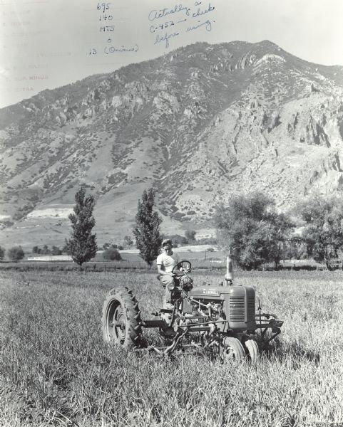 Three-quarter view from front right of Robert C. Taylor working as a farm operator for his father. Robert is operating a Farmall C tractor with No. C-452 cultivator in a 1-acre field of onions cultivating 4 rows at a time. In the background are mountains.