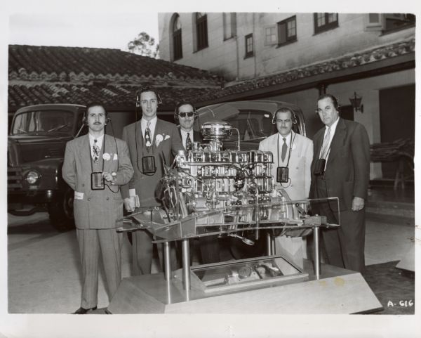 Original caption reads: "Two examples of the modern age of communication and transportation meet in the open air display of new International L-line trucks at the International Harvester Havana Conference as members of various Latin-American distributor firms wearing individual receiving sets gather around the new Silver Diamond valve-in-hand engine displayed as a cutaway working model. The receiving sets are part of the translating-transmitting equipment used at the meeting to give the audience speeches in either Spanish or English simultaneously. Selection of channels on these small radio receiving sets allows easy choice of language."