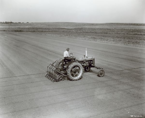 Elevated view of a man using a Farmall C tractor. He is planting carrot in 12-inch rows with a C-635 six-row, rear mounted planter.