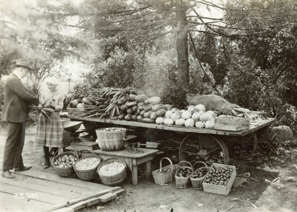 Girl selling vegetables to a customer at vegetable stand along Milwaukee pike. Original caption reads: "The little girl in charge sold over $800 worth of vegetables during the season." Specific location unknown.