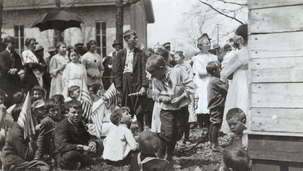 Farm children, families and other onlookers watch an alfalfa series lecture by J.H. Skinner of International Harvester's Agricultural Extension Department. The lecture took place in Kent County, Michigan.