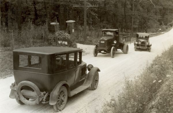 A staged scene showing a car passing a truck while another car is coming the other way. The photograph was taken for International Harvester's Agricultural Extension Department and was used in its campaign to make families aware of farm and home hazards. The original caption reads: "Danger of turning out directly back of truck going up hill."