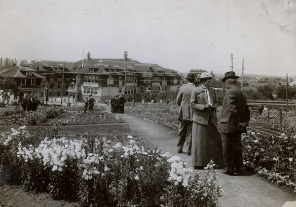 View of groups of men and women looking at the school garden. Below the gardens is the school building.
