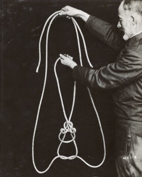 Man standing and displaying a length of rope he has tied with knots.