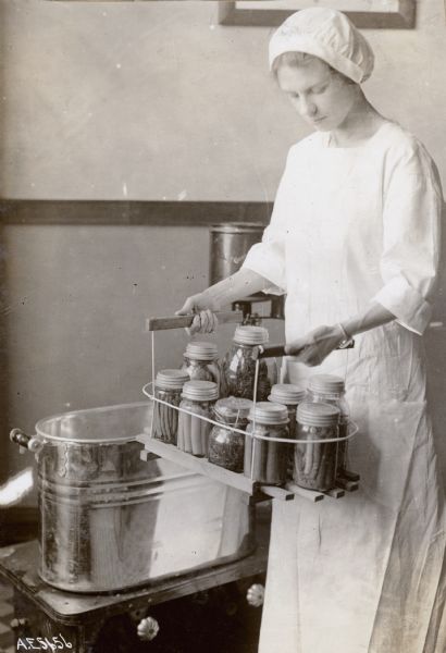 View of a woman holding a canning rack full of jars while standing next to a tub.