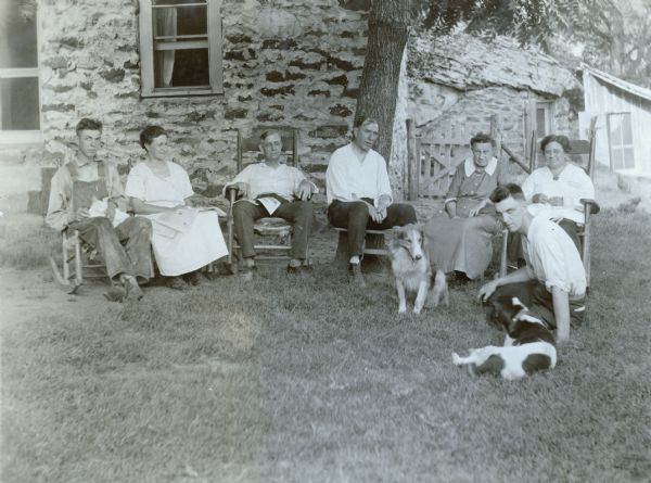 Mr. Mobley and his family posing on the lawn while sitting in chairs or in the grass in front of a house. There are two dogs in the grass, and one of the men is holding a cat in his lap.