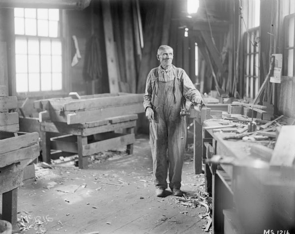 Carpenter standing with his hand on a C. Parker bench vise attached to a work bench at International Harvester's McCormick Works. The McCormick Works was built by Cyrus McCormick in 1873 and became part of International Harvester in 1902. The factory was located at Blue Island and Western Avenues in the Chicago subdivision called "Canalport." It was closed in 1961.