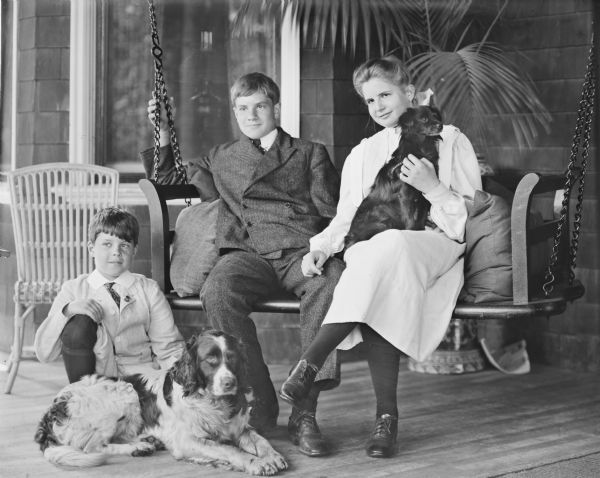 Group portrait on porch of the three children of Cyrus Hall McCormick, Jr. (1859-1936), and his wife, Harriet Bradley Hammond (1862-1921). Pictured, left to right, with two pet dogs are: Gordon (1894-?) kneeling, Cyrus III (1890-1970), and Elizabeth (1892-1905) sitting in a porch swing.