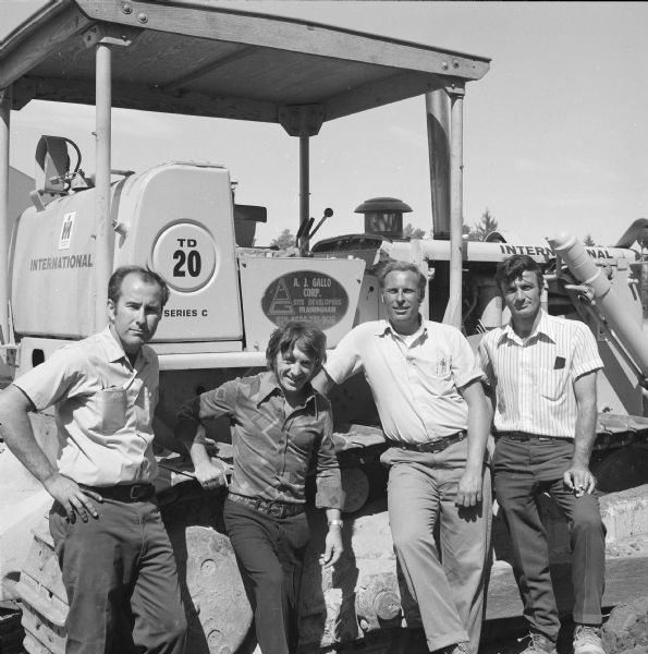 Group of four men posing outdoors in front of a TD-20C Crawler Dozer. A decal on the dozer reads: "A.J. Gall Corp., Site Developers, Framingham."