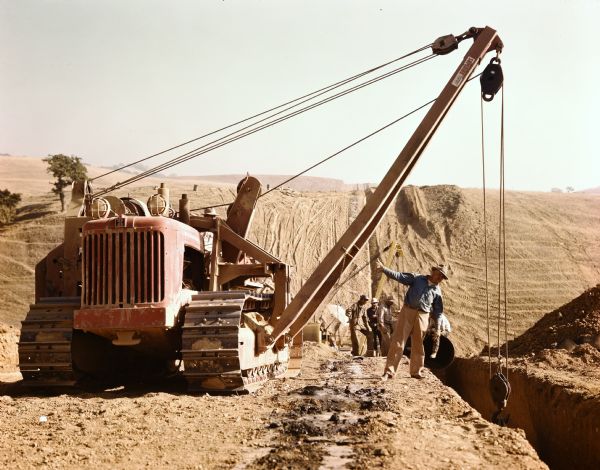 A group of men are working with an International crawler tractor (TracTracTor) with a crane.
