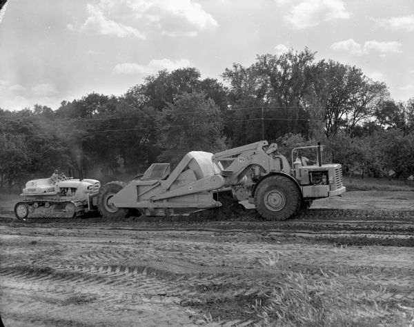 Right side view of a man operating a Euclid TC-12 behind a man operating a 295 Pay Scraper in a field.
