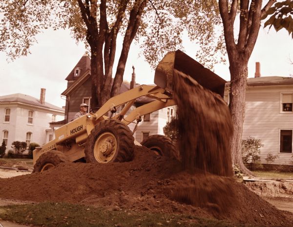 Man operating a Hough Pay Loader to move earth. Houses are in the background.