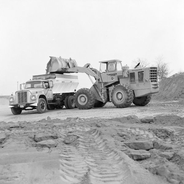 Man operating a Hough 90 Pay Loader to dump material into an International truck.