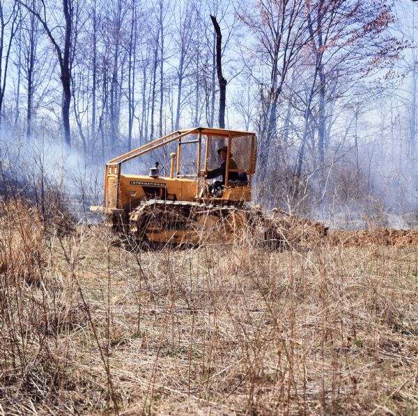 Left side view of a man operating a 500 Pay Dozer. The trees and ground in the background are black, and there is smoke.
