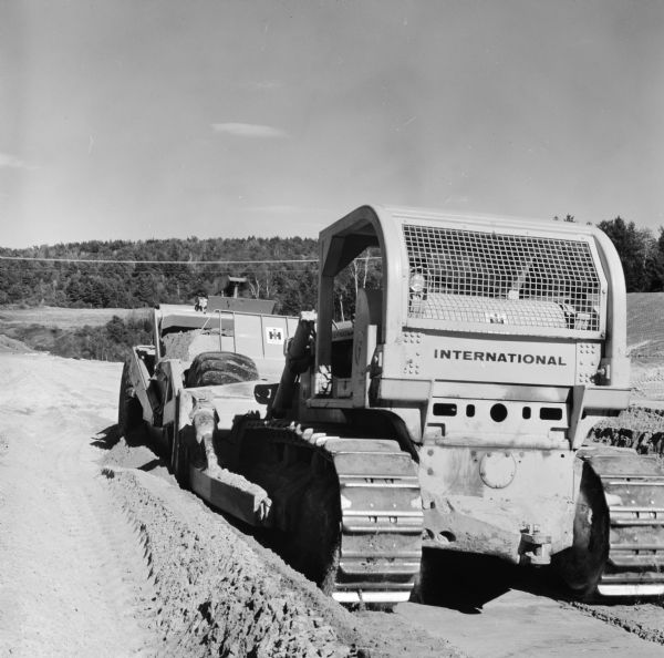 Three-quarter view from left rear of a man operating a TD-25 behind a Pay Scraper. Caledonia, Inc., has contract to construct a section of Interstate I-91.
