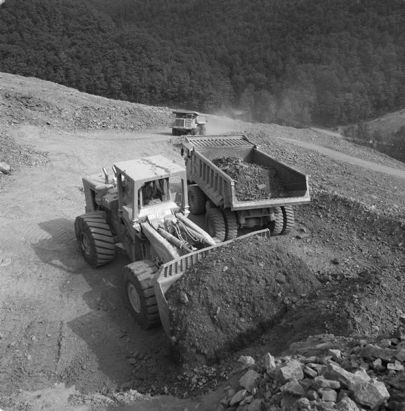 Elevated view of men operating Pay Haulers and a Pay Loader at the top of a hill. Vecellio and Grogan, Inc., working on highway project cutting four and one-half miles of Interstate through the rugged terrain of Brushy Mountain.