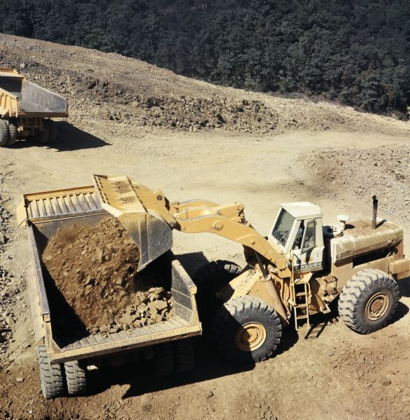 Elevated view of a man operating a Pay Loader to load a Pay Hauler with dirt. Vecellio and Grogan, Inc., working on highway project cutting four and one-half miles of Interstate through the rugged terrain of Brushy Mountain.