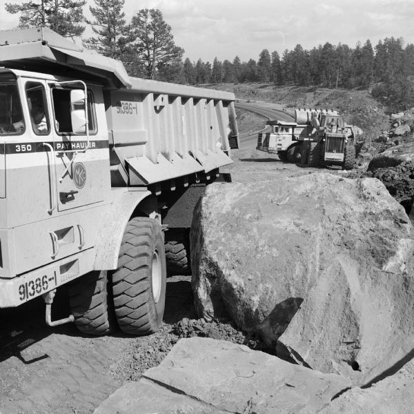 In the foreground is a man in a 350 Pay Hauler. In the background a Hough Pay Loader is loading material into another 350 Pay Hauler. Morrison-Knudsen Co., Inc. and Gordon H. Ball, Inc., a joint venture have a contract to construct south-bound lane of Interstate 17.