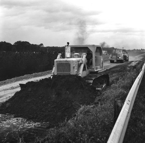Three-quarter view from front left of a man operating a TD-25 to move earth. Shepherd Construction Company, Inc., has sub-contract for grading and drainage work on section of Georgia Route 333.