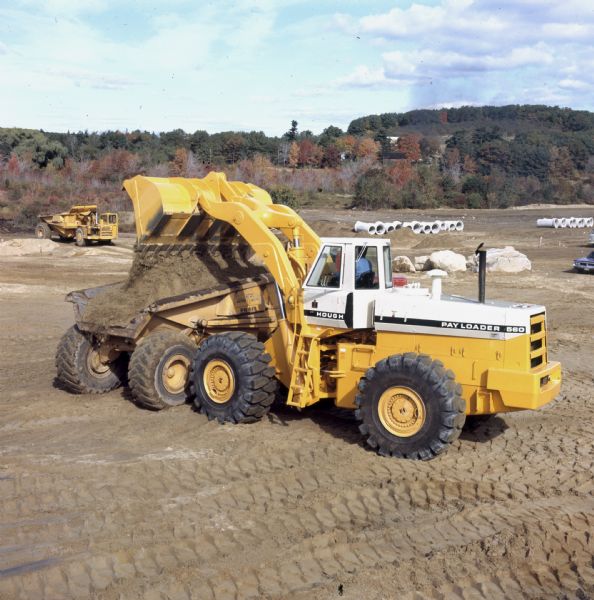 Slightly elevated view of a man operating a 560 Hough Pay Loader. C&M Enterprises, excavation contractors, are using two Hough Pay Loaders: a new 560 and a two-year-old H90e. Contract is for site development of Miles Standish Sub-Division.