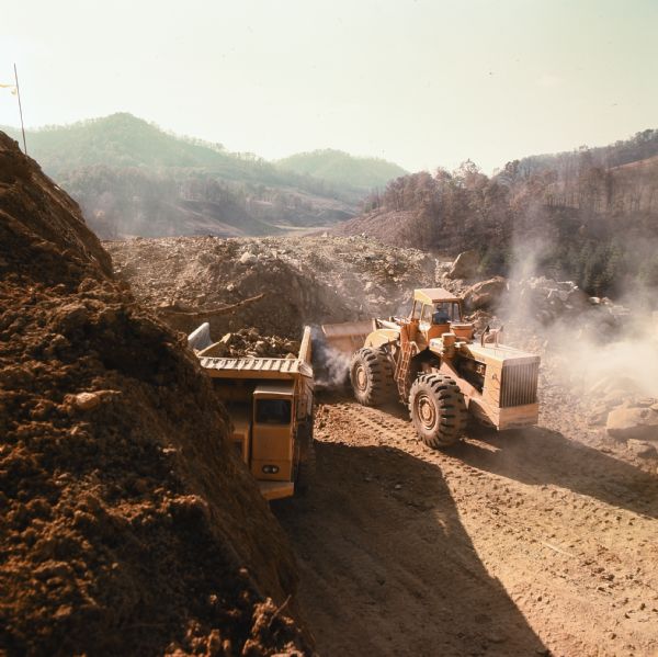 Elevated view of a man operating a Hough H 400 to move rock. On the left is a man operating a PH 180 (T50). L.R. Skelton and Company has contract to construct 3.25 miles of Interstate I-79 in Clay County. Right-of-way for this project is in rugged mountain terrain.