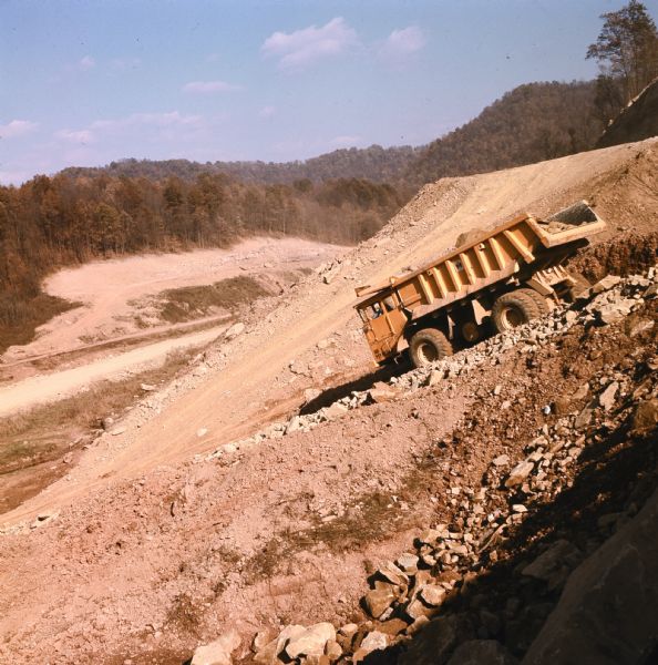 Man operating a PH 180 (T50) down a steep grade, trees visible in the background. L.R. Skelton and Company has contract to construct 3.25 miles of Interstate I-79 in Clay County. Right-of-way for this project is in rugged mountain terrain.