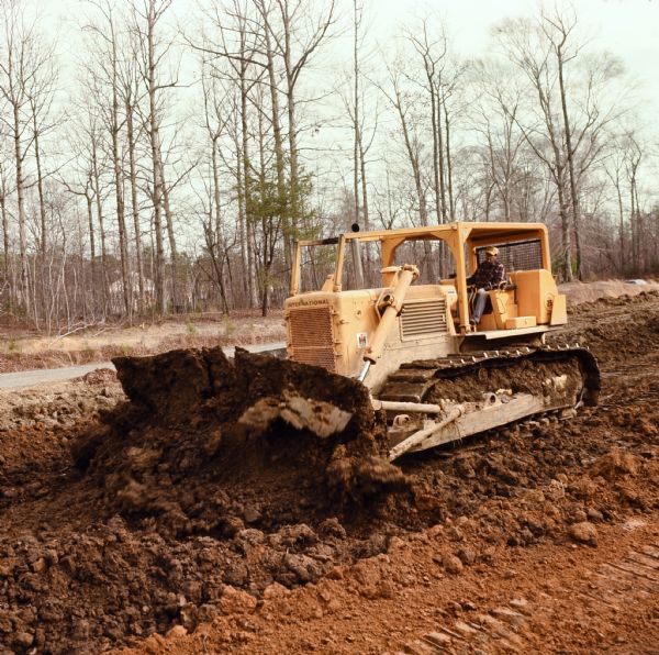 Man operating TD25c Dozer to move earth. Caption reads: "Williams Paving Company has contract to reconstruct and relocate 2.686 miles of route US 60 in Newport News."