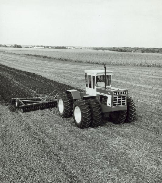 Elevated view of man driving an International 4366 Turbo in a field pulling an agricultural implement. Farm buildings are in the background.