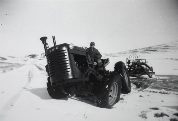 Man driving International four-wheel drive tractor in the snow.