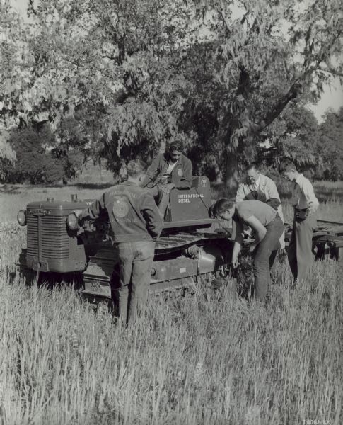 Students in Future Farmers of America learning in a field. Original caption reads: "E.W. Gills, F.F.A. advisor (in white duster) explaining proper lubrication of International TD-6 crawler tractor and Dyrr offset disk harrow to some of his Future Farmers of Atascadero, California.