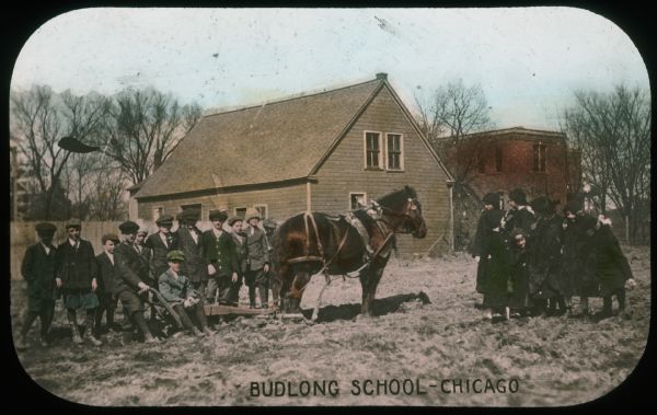 View of children gathered around a horse-drawn walking plow at Budlong School. Hand-tinted lantern slide.